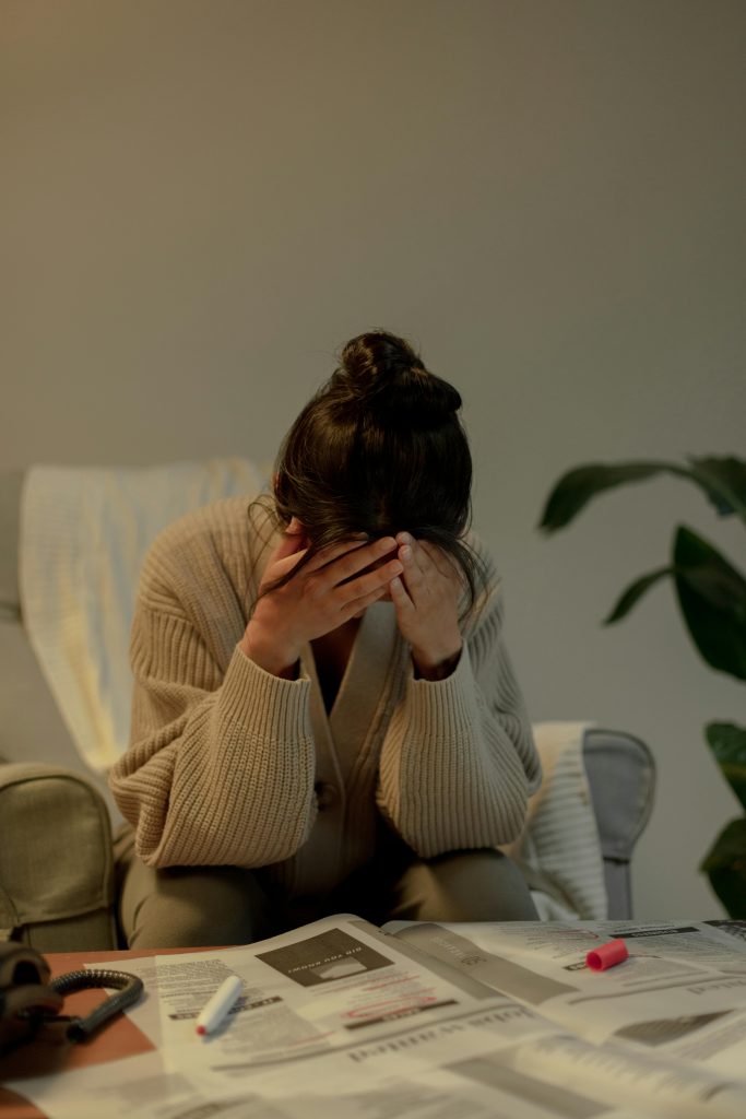 A woman in a sweater shows stress over job search documents at home.